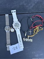 Photo shows three watches including a metal mesh band analog watch, a white plastic digital sport watch, and a small pocket watch, along with several necklaces with pendants including a gold-tone chain, a 'SAVAGE' pendant, and cross pendants on colored cords.