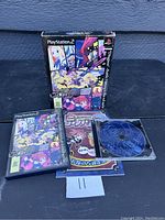 Photo shows Disgaea PS2 game case, manual, and disc spread out on a dark surface.