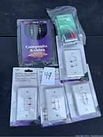 Photo of Composite S-Video cable in packaging, four white plastic wall plates with integrated heavy-duty brackets, and small sealed packs of electrical wire terminals.