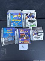 Photo showing two boxed Gameboy Advance games: Pong Asteroids and Madden 2002, including game cartridges and manuals.
