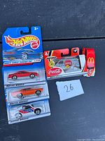 Photo showing three Hot Wheels die-cast cars in packaging and one Coca-Cola themed die-cast car with McDonald's branding, all packaged.
