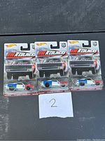 Three Hot Wheels Redliners 75 Dodge Charger R/T diecast cars, sealed in original packaging, arranged horizontally with a handwritten number '2' below.