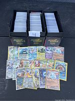 Three black Zenith booster box storage boxes filled with Pokémon trading cards, some holographic and rare cards displayed in front.
