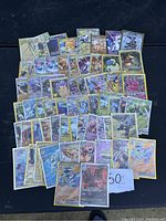 Photo showing 57 rare Pokémon cards laid out in rows on a dark surface with a handwritten "50" card included.