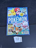 Photo of The Ultimate Guide to Pokemon book cover featuring Pikachu, Ash Ketchum, Eevee, and other Pokemon characters. Shows condition and special collectible insert mention.