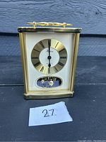 Close-up of gold-tone rectangular quartz clock with roman numeral dial and rotating pendulum visible below clock face.
