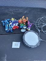 Photo showing the Skylanders Portal of Power with its cable and six associated figurines arranged on a black surface.