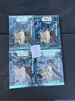 Four sealed booster packs of Star Wars Trading Card Game featuring Attack of the Clones characters, arranged on a black surface.