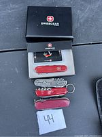 Photo showing four Swiss Army knives with red handles and one silver keychain multi-tool, one knife in SwissGear box.