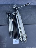 Photo showing three different vintage camera tripods placed on a black surface with a note indicating number 40.