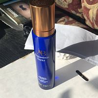 Blue Augustinus Bader 100 ml cleansing gel bottle with gold cap, text detailing product name and volume, placed on white surface with background objects.