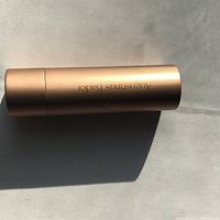 Single rose gold lip balm tube lying flat showing Augustinus Bader branding on side.