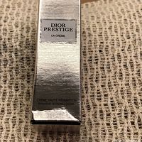 Close-up image of the front of the silver box packaging showing Dior Prestige La Crème branding and product type as Intensive Repairing Cream
