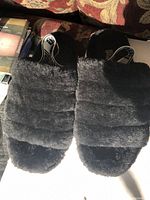 Top view of pair of black fuzzy UGG slippers showing wide padded band and elastic logo strap.