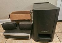 Bose 321 home theater system components including subwoofer, bookshelf speakers, and control unit arranged on a tiled floor.