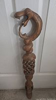 Full view of cobra head hand carved wooden walking stick leaning against a door, showing carved details and length.