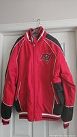Front view of red and black reversible Tampa Bay Buccaneers jacket showing front team logo, zipper closure, and ribbed collar and cuffs.