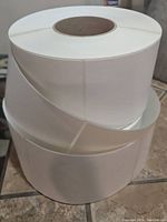 Two rolls of brand new white direct thermal labels, each roll wound on a cardboard core, plain rectangular labels 4x6 inches.