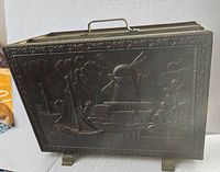 Front view of brass magazine rack showing embossed boat and windmill scene