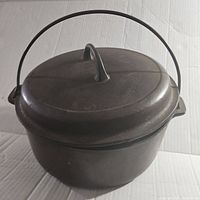 Side view of the vintage cast iron Dutch oven showing the round body, lid with a tall loop handle, and bail handle for carrying.