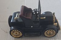 Side view of the black and gold vintage Ford car model lighter showing details of seat, steering wheel, and wheels.