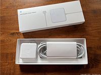 Opened box showing white Apple 60W MagSafe 2 power adapter with attached cable coiled and placed in original packaging.