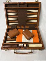 Closed wooden case open showing felt backgammon board, leather dice cups, checkers arranged in trays, and dice.