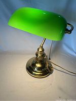 Front side view of bankers desk lamp with emerald green curved glass shade and polished brass base, showing pull chain and flexible neck.