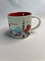Side profile of white ceramic Starbucks Canada You Are Here coffee mug with colorful Canadian-themed graphics and red interior.