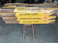 Four boxes of Golden Select Click Laminate Flooring stacked, showing branding and product features on box sides.