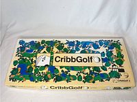 Box top showing CribbGolf game board layout with colorful golf-themed design and CribbGolf logo.