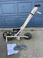 Full side view of the Earthway garden seeder showing frame, wheels, seed box, seed plates on ground and instruction manual nearby.