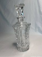 Clear glass decanter standing upright showing detailed faceted glass pattern and stopper fitting on top.