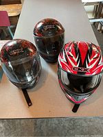 Front view of three helmets on table showing visored youth helmets and red adult helmet without visor.