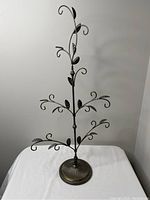 Front view of metal tree necklace stand with decorative leaves and curved branches on a circular base.