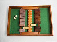Wooden Shut the Box game setup with dark and light numbered tiles and two dice on green felt inside wooden frame.