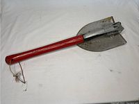 Side view of the folding entrenching tool showing the shovel blade with pick and red handle.