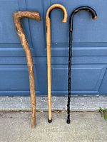 Three vintage canes leaning against a blue garage door showing overall design and handle shapes.