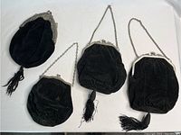Overview photo showing four black velvet handbags arranged flat, featuring metal frames, chain handles, and tassels on some.