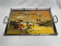 Top view of rectangular serving tray showing reverse painted glass with detailed oriental scene containing traditional buildings, mountain, water, and trees in warm tones.