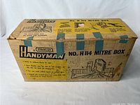 Photo of original cardboard box with Stanley Handyman branding and product name No. H 114 Mitre Box, showing age wear.