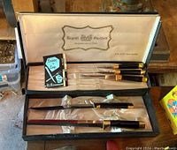 Full view of the Regent Sheffield cutting utensil set in its display case showing six pieces with gold accents and black handles.