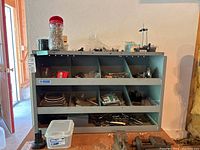 Full view of blue metal shelving unit filled with assorted hardware items, a Washington model 20-005-5 stand on floor, and various containers of small parts.