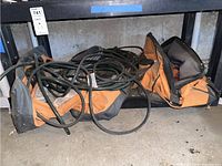 Orange and black tool bag holding multiple long black electrical cords loosely coiled and piled.