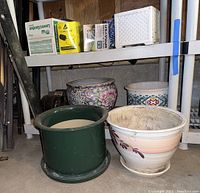 Five ceramic planters of different sizes and patterns placed on floor and shelf in garage.