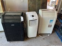 Three floor-standing portable air conditioners side by side: black Everstar, white LG, white Commercial Cool with visible labels and cords.