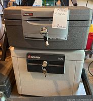 Two Sentry safes stacked: upper safe is F2300 model, fireproof and waterproof, gray and black with key in lock; lower safe is gray Sentry model 1170 with key in lock, showing minor wear and dust.