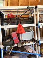 Photo showing shelving with black plastic stacking crates, scrap metal rods, tires, red pouch bag, and a white plastic bin under the shelving