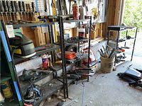 Photo of three metal utility shelf units in a garage setting with tools and equipment on and around them.