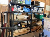 Photo showing two black metal utility shelving units filled with various items in a garage setting.